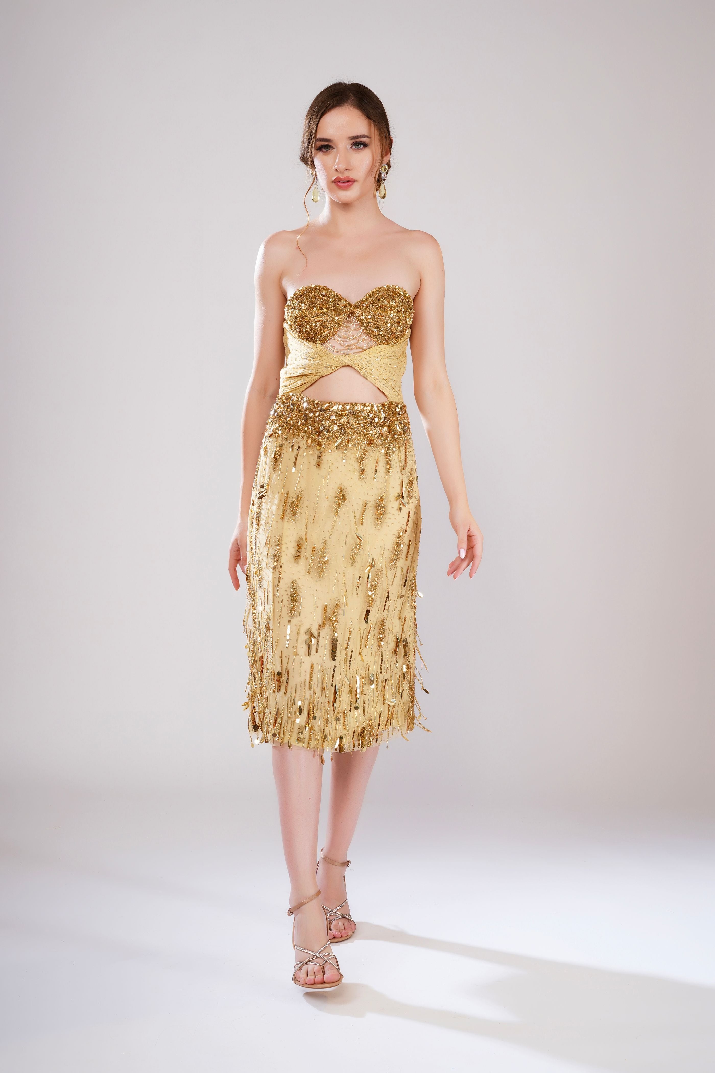 Woman wearing a gold strapless dress with fringe details on a white background